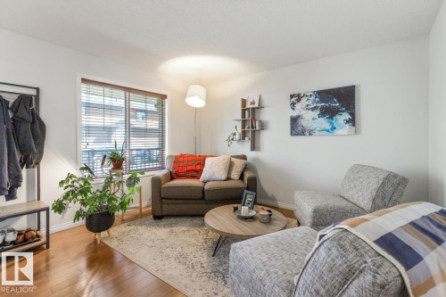 Living area featuring wood-finish flooring, a large window with horizontal blinds, neutral wall tones, and a built-in wall shelf - 7641 Schmid Crescent, Edmonton, AB - Indoor Photo Showing Living Room