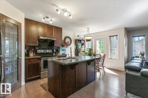 Open-concept kitchen with wood-finish flooring, dark wood cabinetry, and stainless steel appliances - 7641 Schmid Crescent, Edmonton, AB - Indoor Photo Showing Kitchen With Double Sink