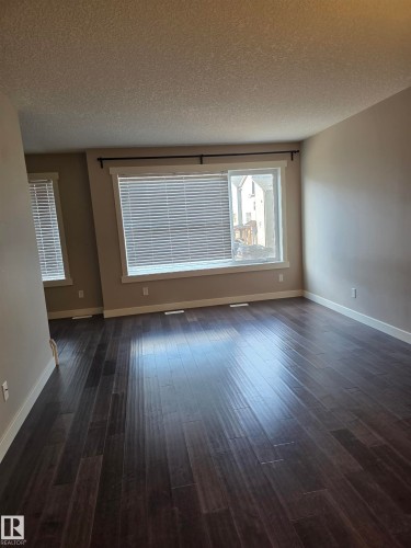 Spacious room featuring dark wood-finish flooring, two large windows with blinds, and neutral painted walls - 295 401 Southfork, Leduc, AB - Indoor Photo Showing Other Room