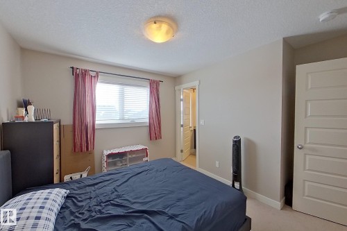 Neutral-toned bedroom featuring a single window with blinds and red drapery panels - 295 401 Southfork, Leduc, AB - Indoor Photo Showing Bedroom