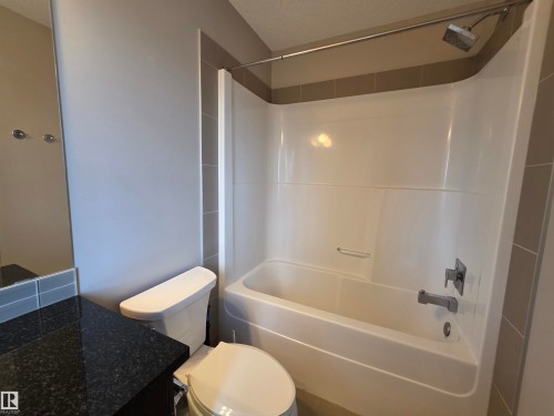 Bathroom featuring a white tub and shower combination with a curved shower curtain rod, a toilet, a dark speckled countertop, and a vanity mirror - 295 401 Southfork, Leduc, AB - Indoor Photo Showing Bathroom