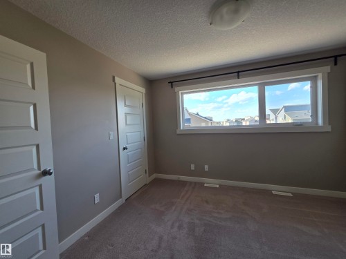 Bright interior space featuring a wide window with white trim, tan carpeting, and light gray walls - 295 401 Southfork, Leduc, AB - Indoor Photo Showing Other Room