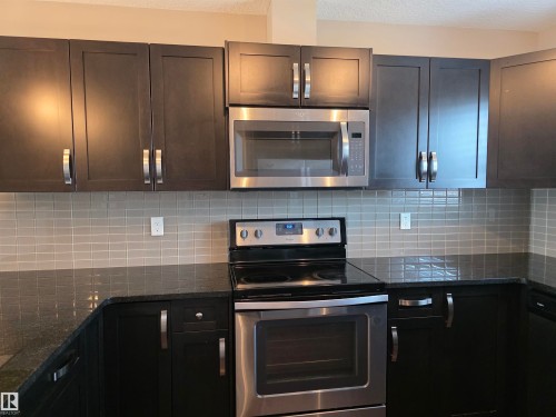 Kitchen featuring dark cabinetry, stainless steel appliances, a tile backsplash, and dark countertops - 295 401 Southfork, Leduc, AB - Indoor Photo Showing Kitchen With Upgraded Kitchen