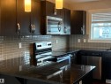 Kitchen featuring dark cabinetry, dark countertops, square tile backsplash, stainless steel appliances, and pendant lighting - 295 401 Southfork, Leduc, AB  - Indoor Photo Showing Kitchen With Upgraded Kitchen 