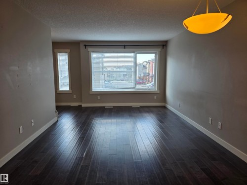 Spacious room featuring dark wood-finish flooring, neutral wall tones, white baseboards, and a contemporary ceiling fixture - 295 401 Southfork, Leduc, AB - Indoor Photo Showing Other Room