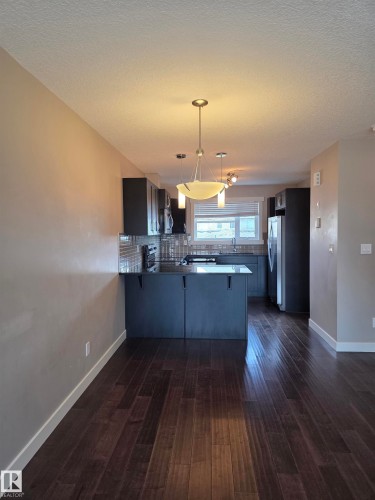 Contemporary kitchen featuring dark cabinetry, stainless steel appliances, a textured tile backsplash, and a breakfast bar - 295 401 Southfork, Leduc, AB - Indoor Photo Showing Kitchen With Upgraded Kitchen