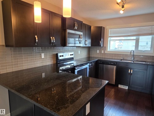 Kitchen featuring dark wood cabinetry, granite countertops, and stainless steel appliances - 295 401 Southfork, Leduc, AB - Indoor Photo Showing Kitchen With Stainless Steel Kitchen With Upgraded Kitchen