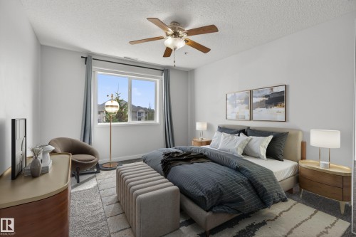 Spacious bedroom featuring light gray walls, a window with a view of residential structures, a ceiling fan with integrated lighting, and carpeted flooring - 319 16303 95 Street, Edmonton, AB - Indoor Photo Showing Living Room With Fireplace