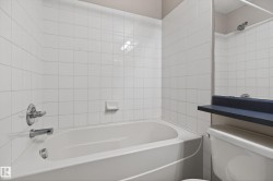 White tiled bath and shower combination with chrome fixtures and a built-in soap dish - 