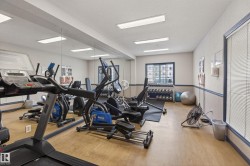 Fitness area featuring wood-finish flooring, full-wall mirror, window with horizontal blinds, track lighting, and a neutral color palette - 