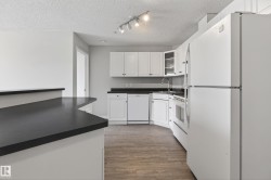 Open-concept kitchen featuring white cabinetry, dark countertops, white appliances, wood-finish flooring, and track lighting - 