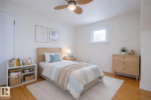 Bright room featuring wood-finish flooring, a white window frame, and a ceiling fan with wood-finish blades - 11507 72 Avenue, Edmonton, AB - Indoor Photo Showing Bedroom