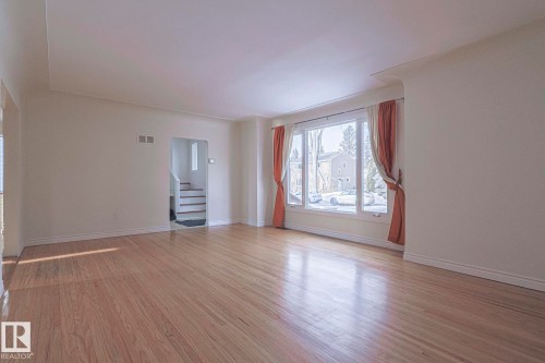 Spacious main living area featuring wide plank wood-finish flooring, a curved bay window with multiple panes, and white baseboards - 11507 72 Avenue, Edmonton, AB - Indoor Photo Showing Other Room