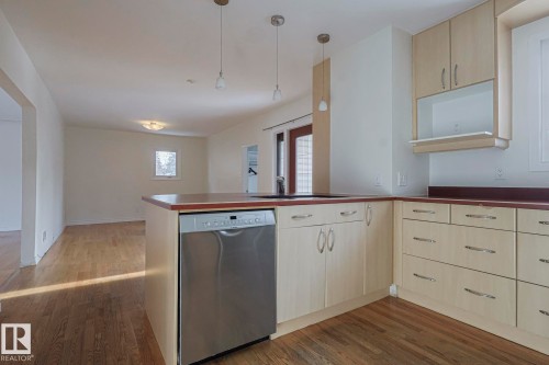 Kitchen featuring light wood-finish cabinetry, dark countertops, a stainless steel dishwasher, and a sink within the island - 11507 72 Avenue, Edmonton, AB - Indoor Photo Showing Kitchen