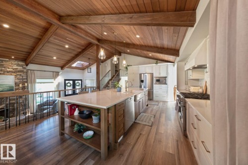 Open-concept kitchen featuring an oversized island with countertop seating, stainless steel appliances, white cabinetry, and wood-finish flooring - 12423 28A Avenue, Edmonton, AB - Indoor Photo Showing Kitchen