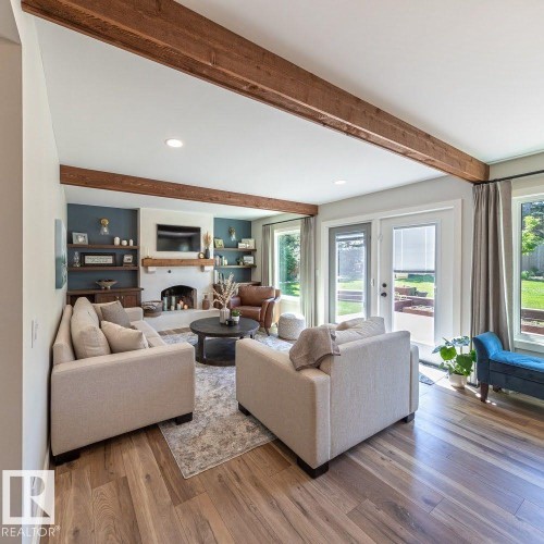 Spacious living area featuring wood-finish flooring, exposed ceiling beams, a white brick fireplace with a wood mantel, and built-in shelving - 12423 28A Avenue, Edmonton, AB - Indoor Photo Showing Living Room