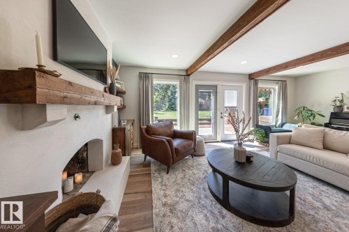 Living area featuring a textured fireplace with a substantial wood mantel, wood-finish flooring, and exposed ceiling beams - 12423 28A Avenue, Edmonton, AB - Indoor Photo Showing Living Room With Fireplace