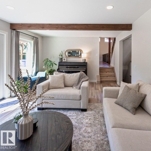 Light-filled living area featuring wood-finish flooring, a prominent exposed wood beam, recessed ceiling lighting, and a large window with privacy drapes - 12423 28A Avenue, Edmonton, AB - Indoor Photo Showing Living Room
