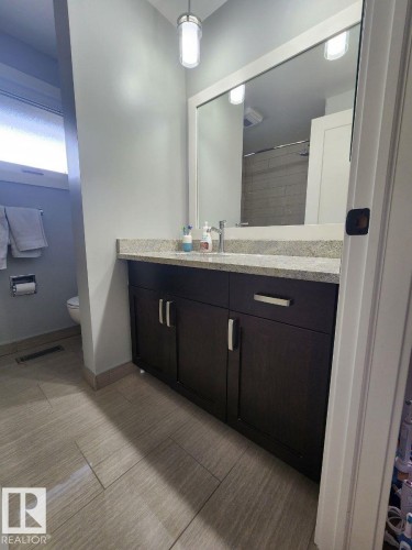 Bathroom featuring a dark wood-finish vanity with a light speckled countertop, under-mount sink, and a large framed mirror - 12423 28A Avenue, Edmonton, AB - Indoor Photo Showing Bathroom