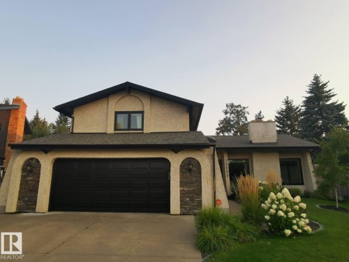 Stucco exterior residence featuring a prominent black garage door, stone veneer accents, and a contrasting dark roof - 12423 28A Avenue, Edmonton, AB - Outdoor