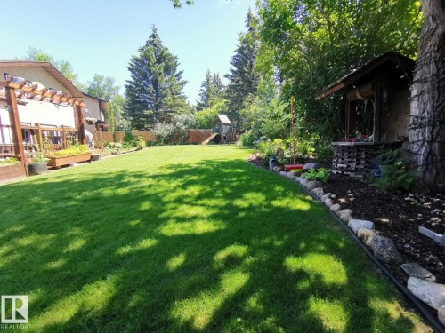 Expansive backyard featuring a lush lawn, mature trees, a multi-level wood deck with a pergola, raised garden beds, and a decorative garden structure - 12423 28A Avenue, Edmonton, AB - Outdoor