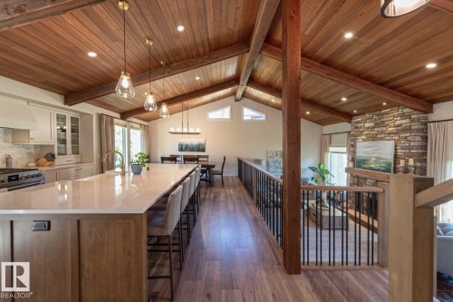 Vaulted wood-plank ceilings with exposed beams, wood-finish flooring, a stone-clad fireplace, and a kitchen island with a light-toned countertop - 12423 28A Avenue, Edmonton, AB - Indoor Photo Showing Kitchen With Upgraded Kitchen