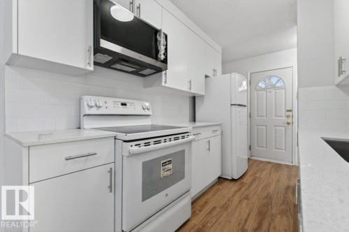 Kitchen featuring white flat-panel cabinetry, light-toned countertops, a white subway tile backsplash, and wood-finish flooring - 3E Twin Terrace, Edmonton, AB - Indoor Photo Showing Kitchen