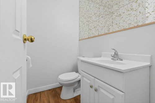 Compact powder room featuring a white vanity with integrated sink, chrome faucet, wood-finish flooring, and a decorative wall accent - 3E Twin Terrace, Edmonton, AB - Indoor Photo Showing Bathroom