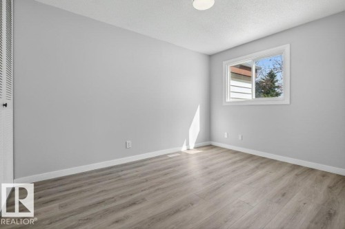 Room featuring a window with white trim, wood-finish flooring, light gray wall paint, and a built-in closet with louvered doors - 3E Twin Terrace, Edmonton, AB - Indoor Photo Showing Other Room