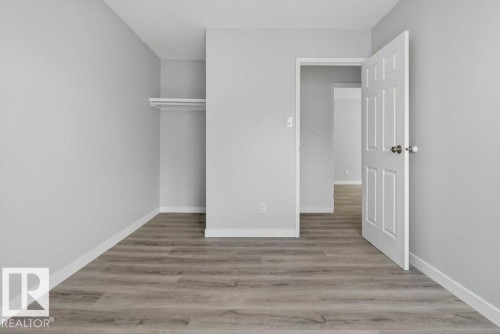 Room featuring wood-finish flooring, light gray walls, white baseboards, and an open closet with shelving and hanging rod - 3E Twin Terrace, Edmonton, AB - Indoor Photo Showing Other Room