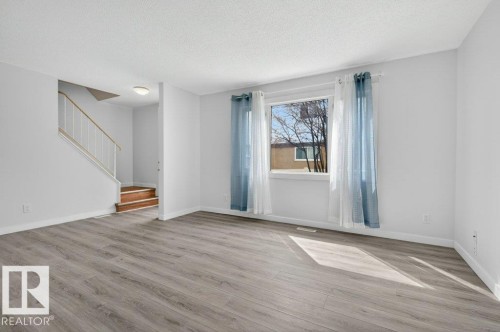 Spacious living area featuring light gray wood-finish flooring, white painted walls, and a large window with white trim - 3E Twin Terrace, Edmonton, AB - Indoor Photo Showing Other Room