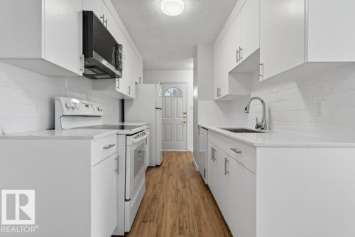 Galley kitchen featuring white cabinetry, light-toned countertops, and wood-finish flooring - 3E Twin Terrace, Edmonton, AB - Indoor Photo Showing Kitchen