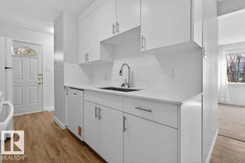 Modern kitchen featuring white shaker cabinetry, light-toned countertops, a stainless steel sink, subway tile backsplash, and wood-finish flooring - 3E Twin Terrace, Edmonton, AB - Indoor Photo Showing Kitchen