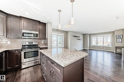 Spacious kitchen featuring dark wood cabinetry, stainless steel appliances, and a central island with a light-toned granite countertop - 10519 114 Avenue, Edmonton, AB - Indoor Photo Showing Kitchen With Stainless Steel Kitchen With Upgraded Kitchen