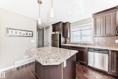 Kitchen featuring an island with a speckled countertop, dark wood-finish cabinetry, stainless steel appliances, and wood-finish flooring - 10519 114 Avenue, Edmonton, AB - Indoor Photo Showing Kitchen With Upgraded Kitchen
