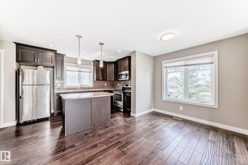 Modern kitchen featuring dark wood cabinetry, stainless steel appliances, a center island with a stone countertop, and wood-finish flooring - 10519 114 Avenue, Edmonton, AB - Indoor Photo Showing Kitchen With Stainless Steel Kitchen With Upgraded Kitchen