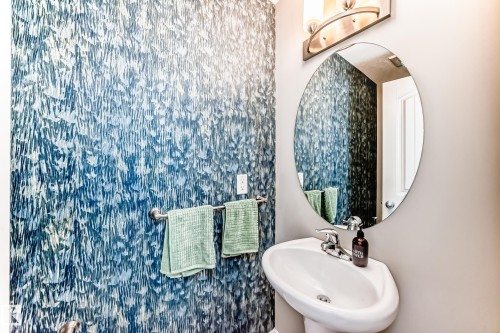 Powder room featuring a pedestal sink with chrome faucet, an oval wall mirror, and a wall-mounted light fixture - 10519 114 Avenue, Edmonton, AB - Indoor Photo Showing Bathroom