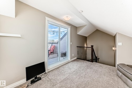 Carpeted loft area featuring a sliding glass door to an outdoor patio with concrete flooring, a dark wood newel post with wrought iron balusters, sloped ceilings, and neutral wall paint - 10519 114 Avenue, Edmonton, AB - Indoor