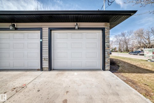Two-car garage featuring paneled doors, stone veneer accents, neutral siding, dark trim, and overhead lighting fixtures - 10519 114 Avenue, Edmonton, AB - Outdoor With Exterior