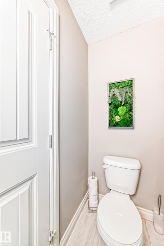 Neutral-toned powder room featuring light wood-finish flooring, a white toilet, and a contemporary decorative wall accent - 10519 114 Avenue, Edmonton, AB - Indoor Photo Showing Bathroom