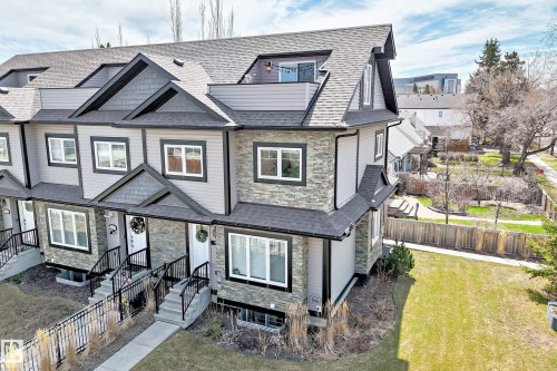 Townhouse exterior featuring light gray siding, dark stone veneer accents, individual front entrances with concrete steps, black metal railings, and a dormer window with a balcony - 10519 114 Avenue, Edmonton, AB - Outdoor