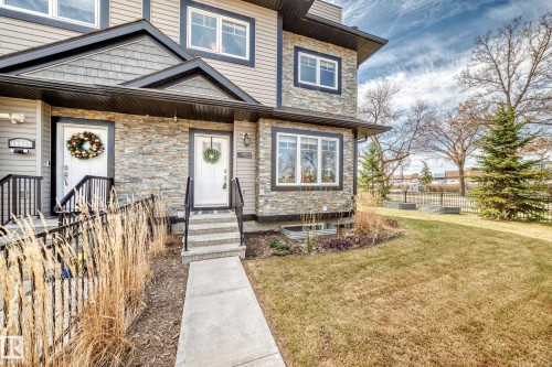 Exterior featuring stacked stone accents, horizontal siding, black trim windows, a concrete walkway, and a landscaped front yard with a mature evergreen - 10519 114 Avenue, Edmonton, AB - Outdoor