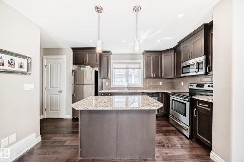 Kitchen featuring a central island with a granite countertop, wood-finish flooring, dark wood cabinetry, stainless steel appliances, and subway tile backsplash - 10519 114 Avenue, Edmonton, AB - Indoor Photo Showing Kitchen With Stainless Steel Kitchen With Upgraded Kitchen