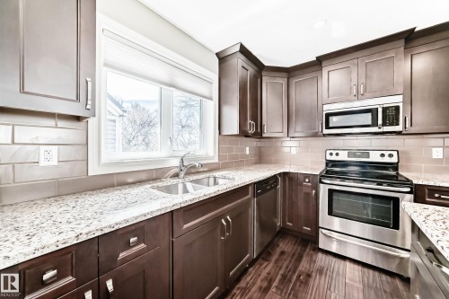 Kitchen featuring wood-finish flooring, dark wood cabinetry, light-toned granite countertops, and a subway tile backsplash - 10519 114 Avenue, Edmonton, AB - Indoor Photo Showing Kitchen With Stainless Steel Kitchen With Double Sink With Upgraded Kitchen