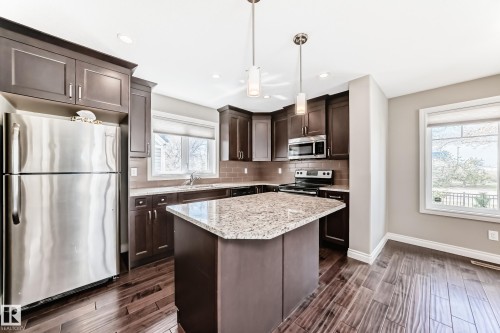 Contemporary kitchen featuring dark wood cabinetry, stainless steel appliances, a center island with a light-colored countertop, wood-finish flooring, and pendant lighting - 10519 114 Avenue, Edmonton, AB - Indoor Photo Showing Kitchen With Stainless Steel Kitchen With Upgraded Kitchen