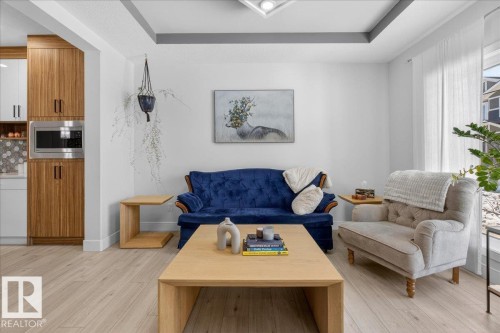 Living room featuring light wood flooring, a tray ceiling, and large windows with sheer white curtains - 1778 25A Street, Edmonton, AB - Indoor Photo Showing Living Room