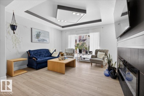 The living area features light-toned flooring, a recessed ceiling with accent lighting, and a modern fireplace with a dark-tiled surround - 1778 25A Street, Edmonton, AB - Indoor Photo Showing Living Room