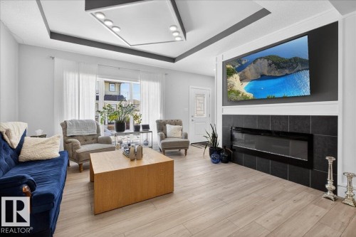 Living room featuring light-toned flooring, a fireplace with dark tile surround, and a decorative ceiling with recessed lighting - 1778 25A Street, Edmonton, AB - Indoor Photo Showing Living Room With Fireplace