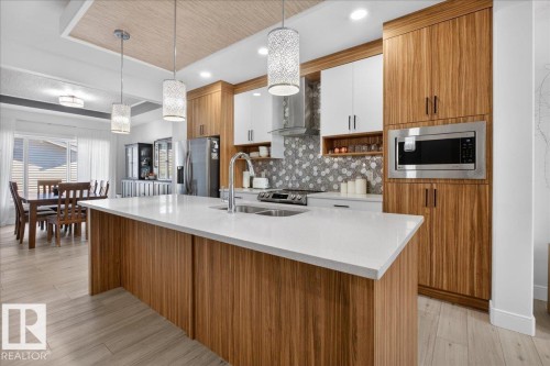 The kitchen features an island with a light-colored countertop, wood grain cabinetry, and recessed lighting - 1778 25A Street, Edmonton, AB - Indoor Photo Showing Kitchen With Double Sink With Upgraded Kitchen