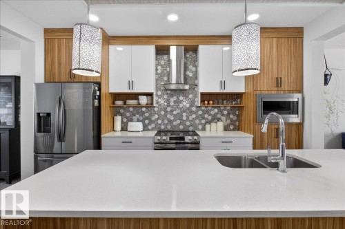 The kitchen features a large island with a double sink, modern appliances, and stylish pendant lighting - 1778 25A Street, Edmonton, AB - Indoor Photo Showing Kitchen With Double Sink With Upgraded Kitchen